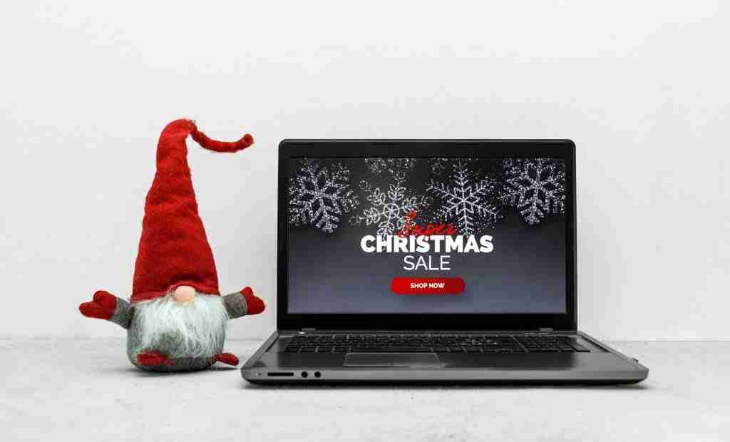 Christmas sale concept with laptop computer and red troll on white backdrop.