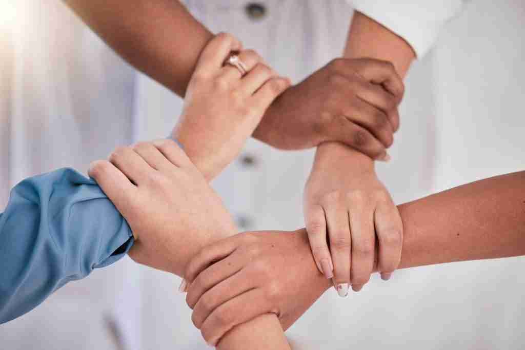 Diverse colleagues hands holding wrists from above in support of unity, loyalty and teamwork in the