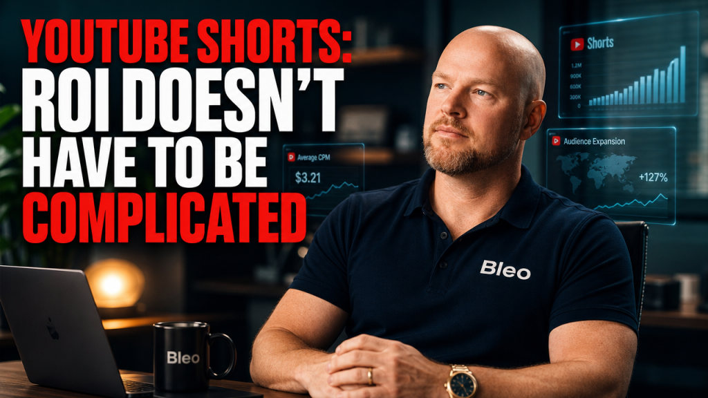 Luke Houlihan sits in a modern office, wearing a Bleo-branded polo shirt, with a confident smile. Behind him are holographic analytics screens showing YouTube Shorts data. A bold title overlay reads "YOUTUBE SHORTS: ROI DOESN'T HAVE TO BE COMPLICATED."